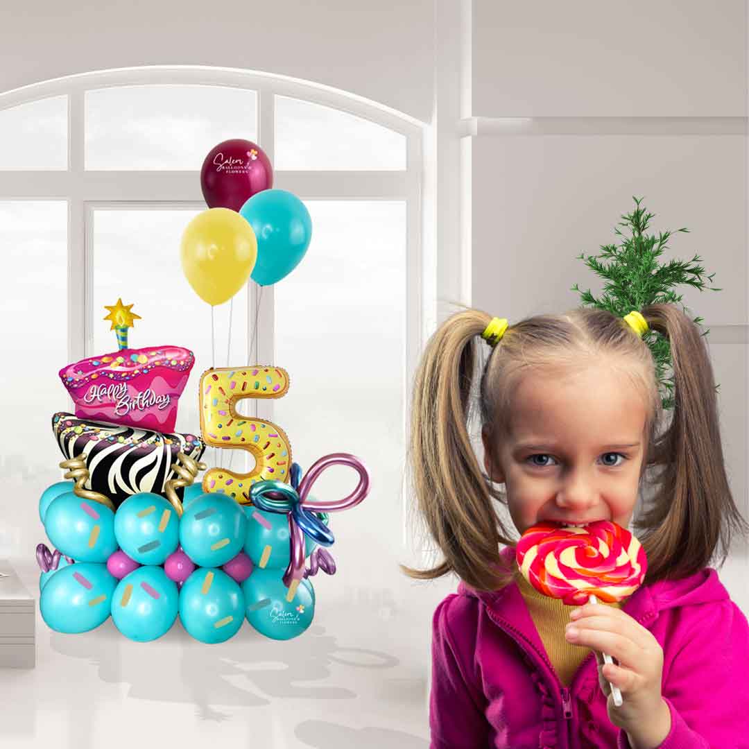 cute girl eating a lollipop standing in front  of a sugar treats themed balloon bouquet with numbers. Balloon delivery in Salem Oregon and nearby cities.