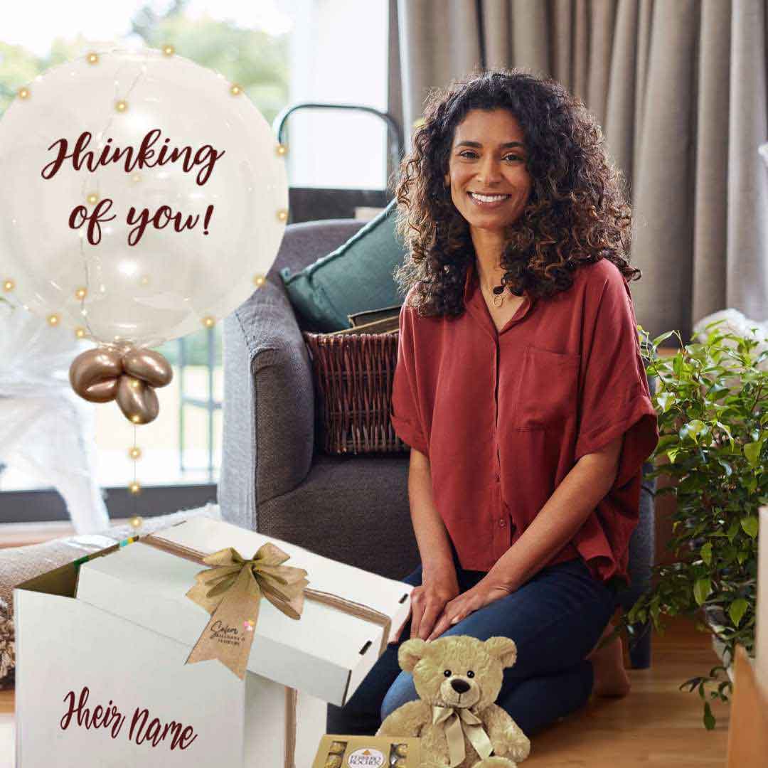 a lady kneeling in front of a Thinking of you balloon box. Filled with a light-up bubble balloon with a "Thinking of You" message, a soft plush and chocolates. Delivery in Salem Oregon and nearby cities.
