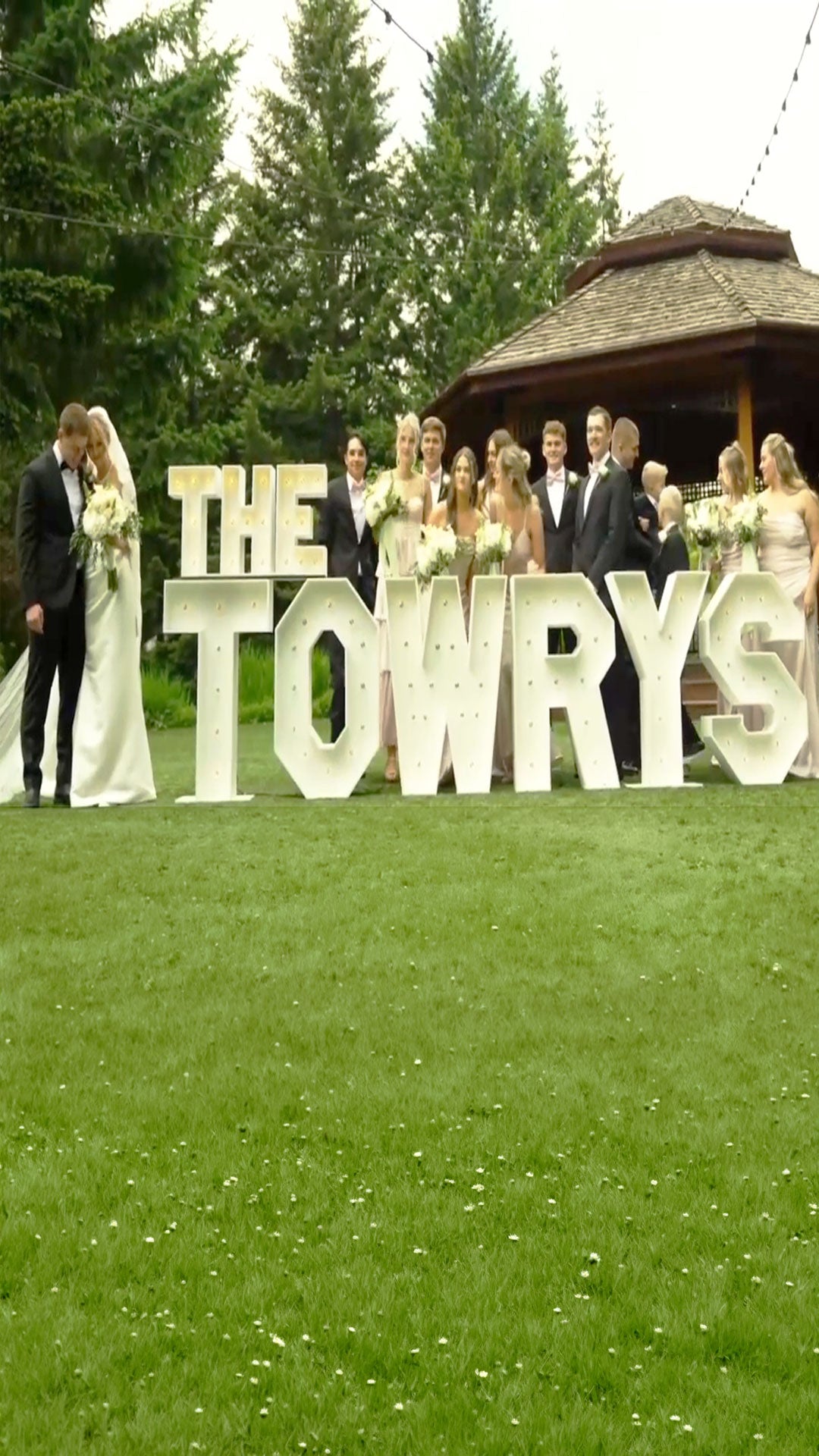 Wedding setup with a large Marquee Letter display spelling "The Towrys" with the newly wedds standing at the left and their wedding company standing behind the marquee Letter display on an outdoors venue by Salem Balloons and Flowers.