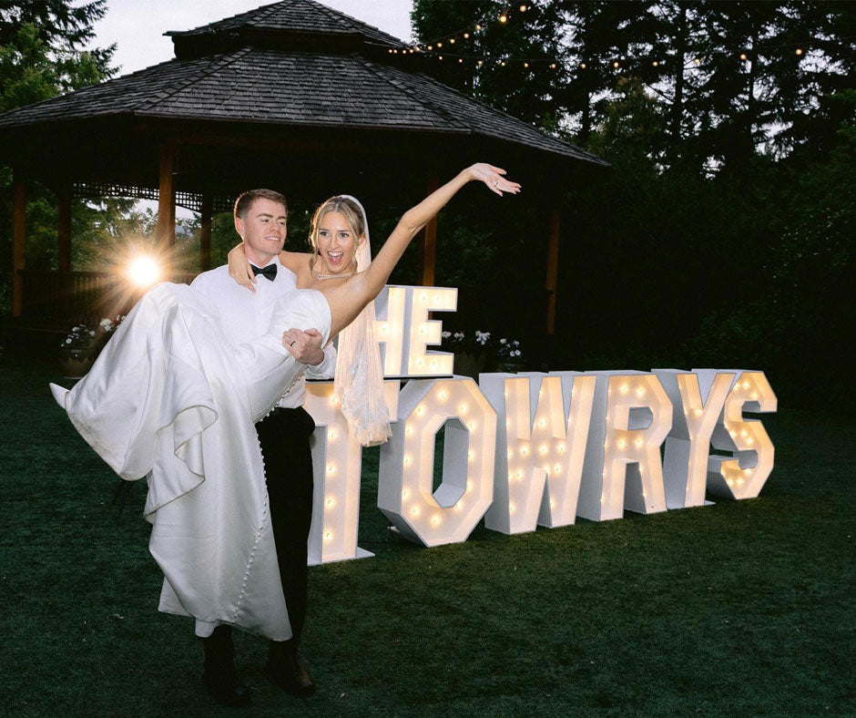 Bride and groom posing in front of illuminated “THE TOWRYS” marquee letters during an outdoor wedding reception at Paradise Springs in Monroe, Oregon. Luxury wedding marquee letter installation by Salem Balloons and Flowers serving Salem, Portland, Eugene, and Oregon’s Willamette Valley.