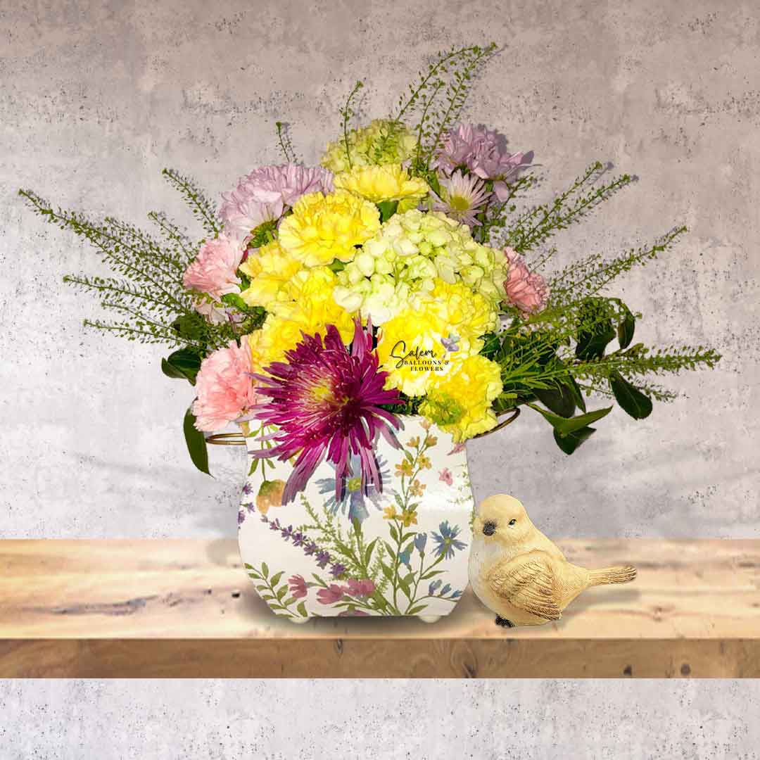 Fresh flowers arranged in a square flower vase in pastel colors and decorated with a bird figurine on a wooden shelf. Salem Oregon Flower delivery
