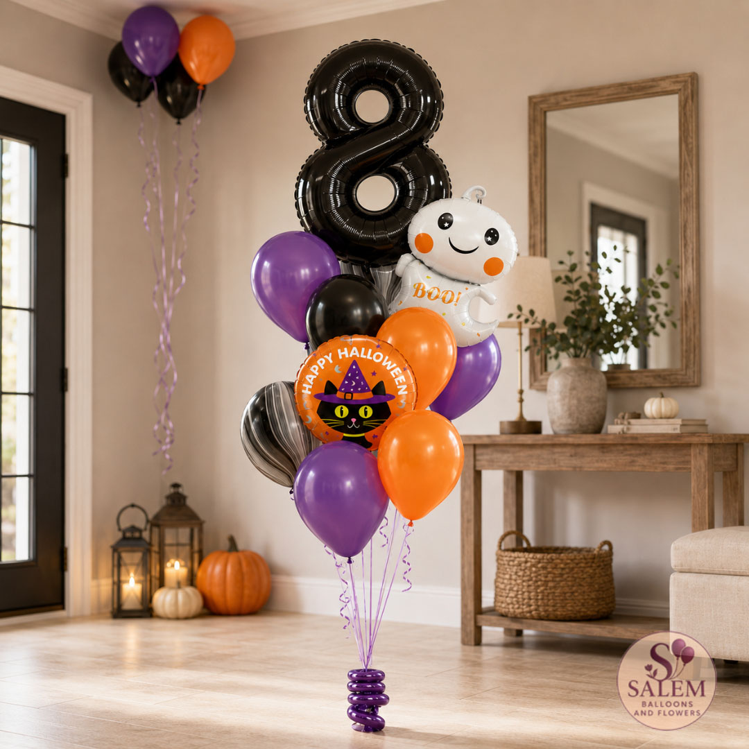 A Halloween-themed balloon bouquet set up indoors on a table, featuring a large black foil balloon shaped like the number 8, purple, orange, black, gray, and white balloons, a round orange 'Happy Halloween' cat balloon, and a white ghost balloon with 'Boo!' text. The room has fall decorations including pumpkins, lanterns, and a mirror.With a Salem Balloons and Flowers logo on the right bottom corner.