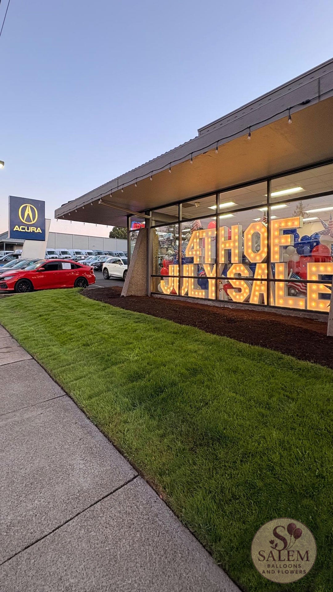 Luxury automotive dealership brand activation at Acura of Salem with illuminated marquee letters, patriotic balloon décor, and custom showroom styling by Salem Balloons & Flowers.