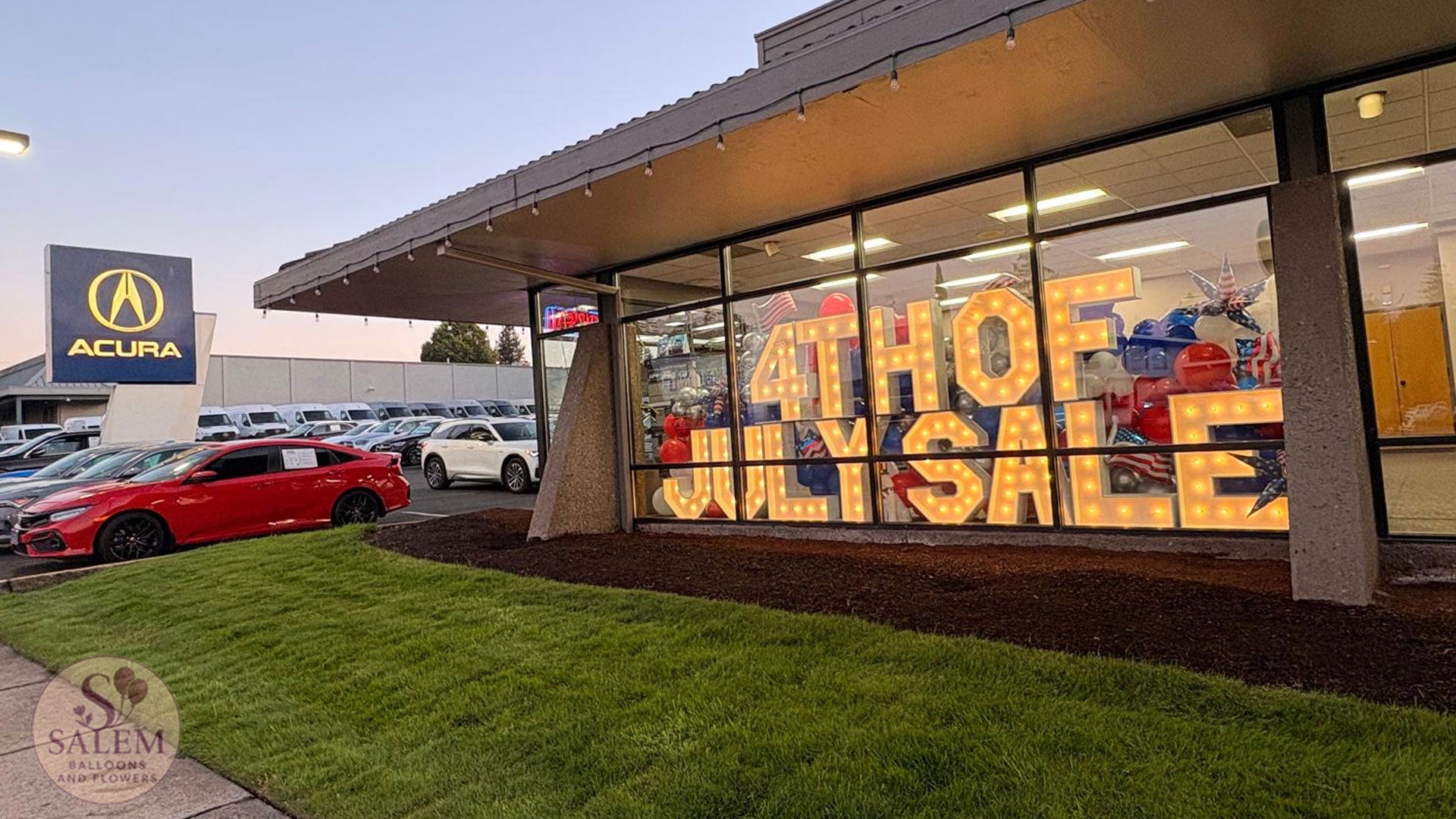 Luxury automotive dealership brand activation at Acura of Salem with illuminated marquee letters, patriotic balloon décor, and custom showroom styling by Salem Balloons & Flowers.