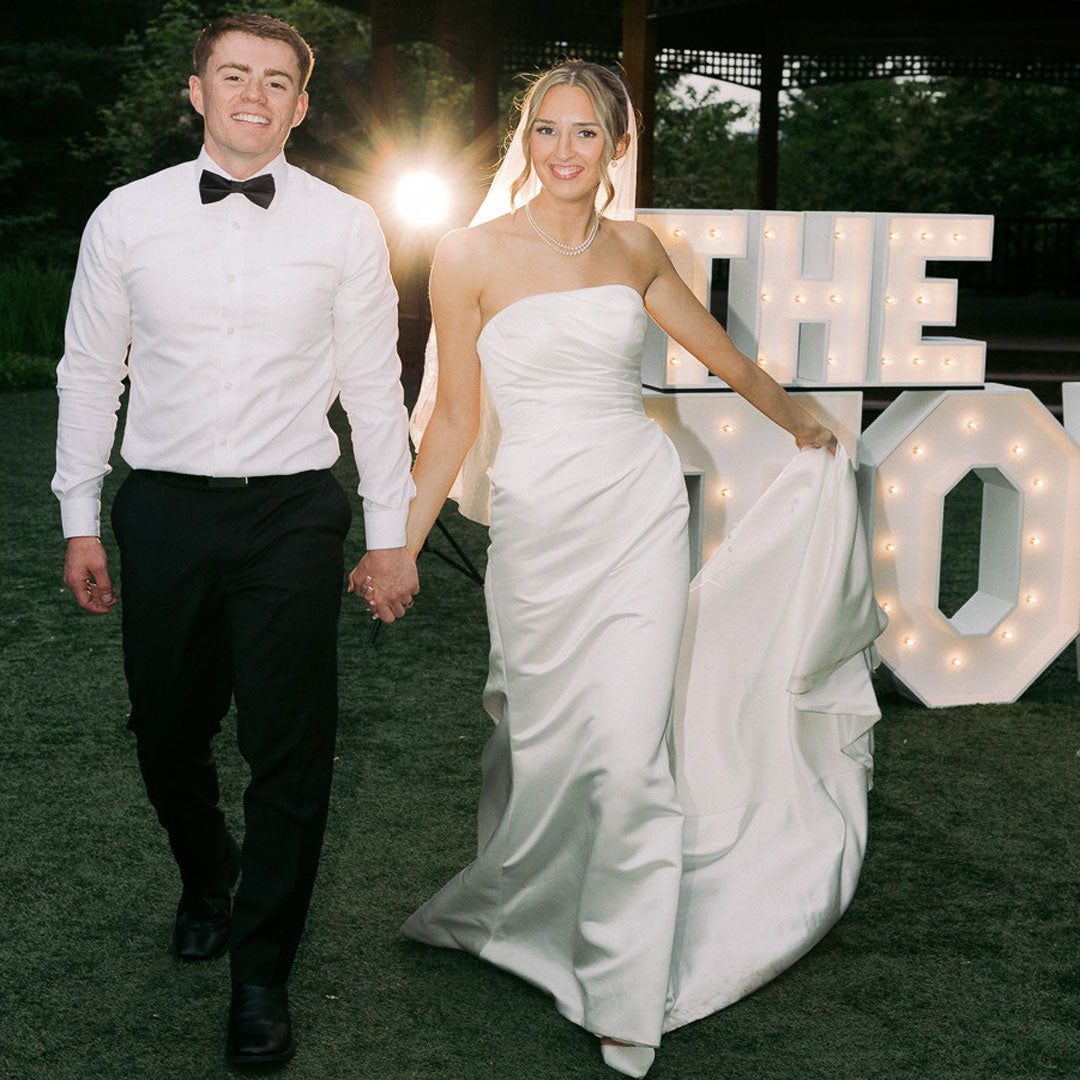 Newlyweds walking in front of custom illuminated wedding marquee letters at an outdoor reception in Monroe, Oregon. Luxury wedding decor and marquee letter installation by Salem Balloons and Flowers.