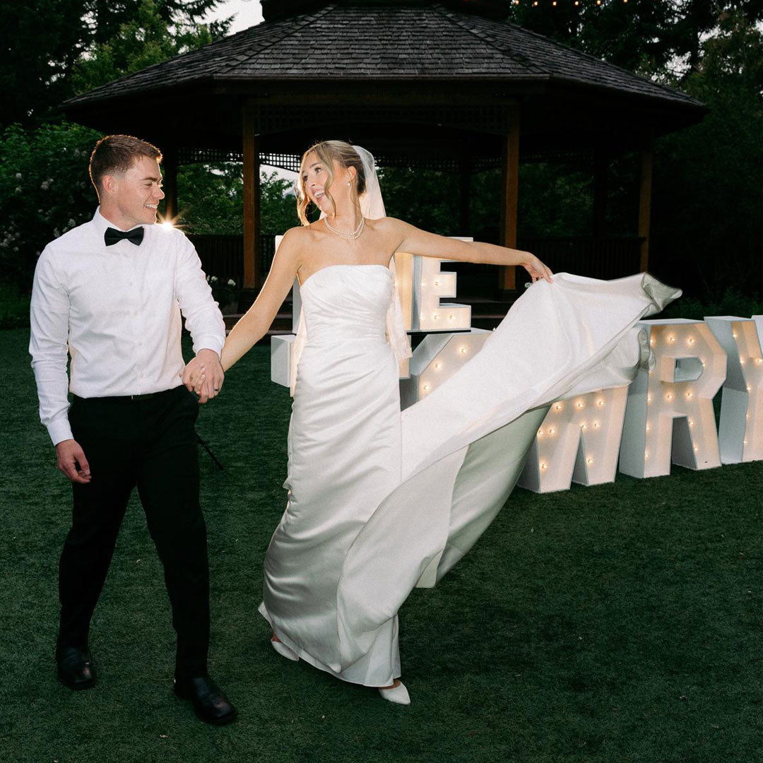 Bride twirling dress beside illuminated wedding marquee letters during a luxury outdoor wedding reception in Oregon’s Willamette Valley. Custom marquee installation by Salem Balloons and Flowers.