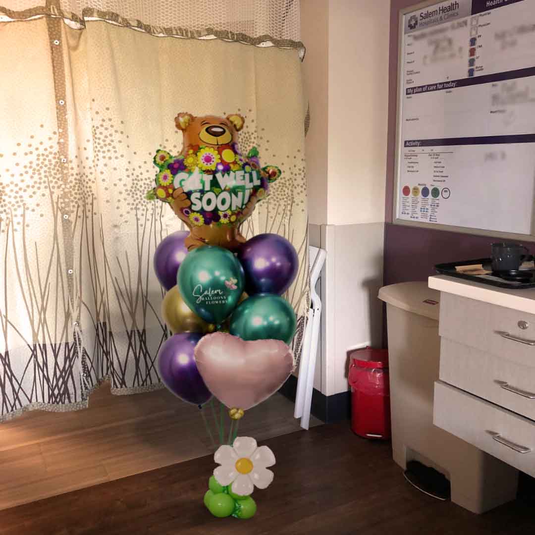A hospital room a Get Well helium balloon bouquet. Featuring a large teddy bear balloon holding flowers with a 