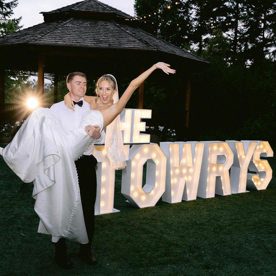 Bride and groom celebrating in front of illuminated “THE TOWRYS” marquee letters during an outdoor wedding reception at Paradise Springs in Monroe, Oregon. Luxury wedding marquee letter installation by Salem Balloons and Flowers serving Salem, Portland, Eugene, and Oregon’s Willamette Valley.