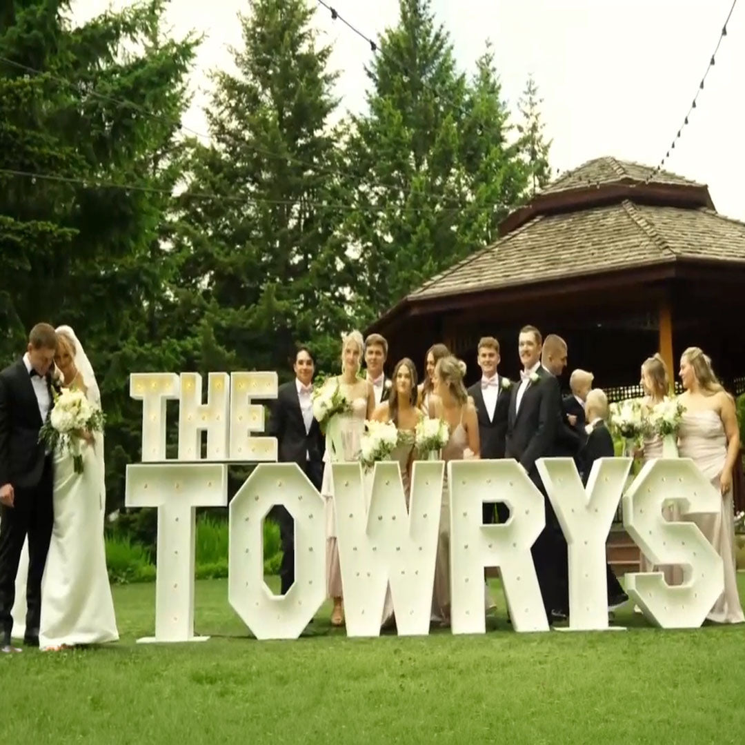 Wedding party gathered around illuminated “THE TOWRYS” marquee letters at Paradise Springs wedding venue in Monroe, Oregon. Luxury wedding marquee display by Salem Balloons and Flowers