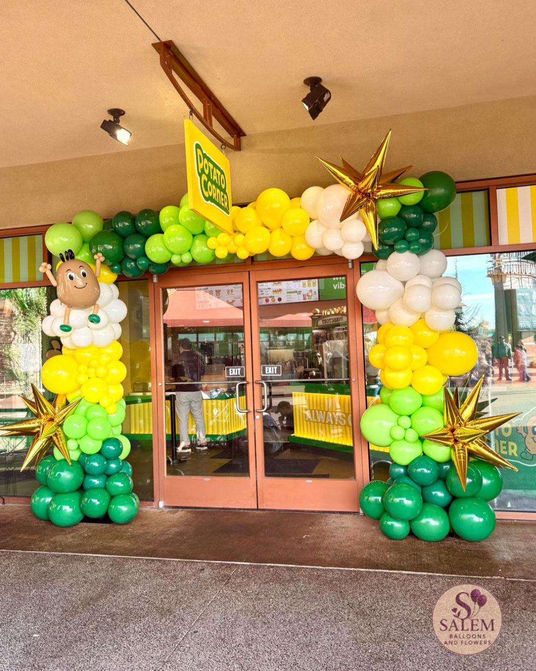 Custom green, yellow and white balloon arch with gold starbursts and handcrafted mascot-inspired sculpture for Potato Corner grand opening at Woodburn Premium Outlets in Oregon.