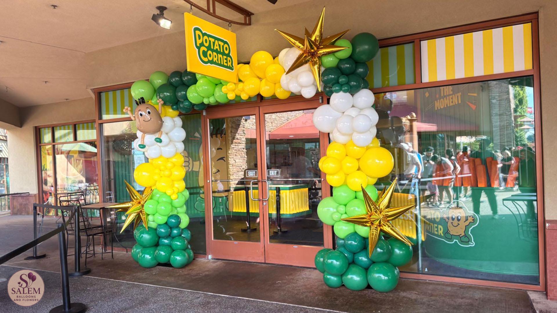 Custom green, yellow and white balloon arch with gold starbursts and handcrafted mascot-inspired sculpture for Potato Corner grand opening at Woodburn Premium Outlets in Oregon.