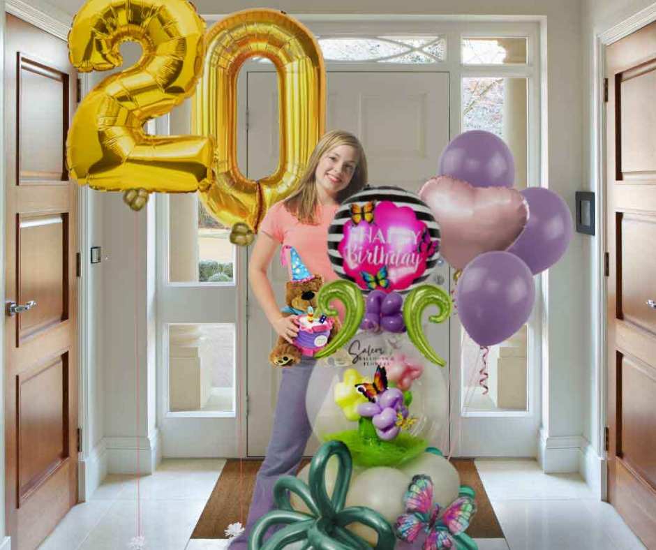 A young girl standing between large helium filled number balloons #20 and a stuffed bubble balloon arrangement filled with flowers and butterflies. Oregon Balloon delivery