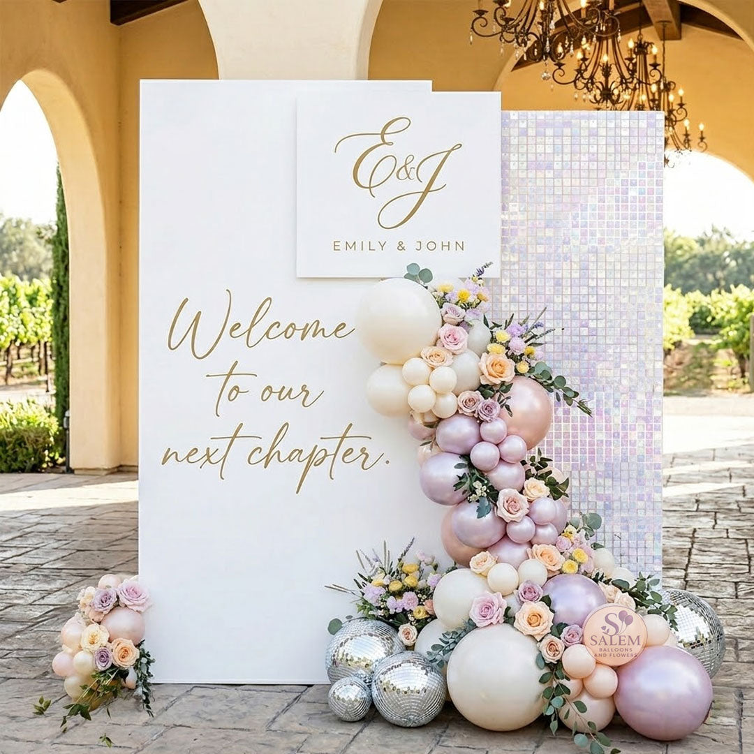A cascading balloon and floral garland in pastel pink, peach, blush, and soft lavender flows down between the panel and a matching white iridescent shimmering sequin wall in a vignard venue. Balloon decor Oregon.