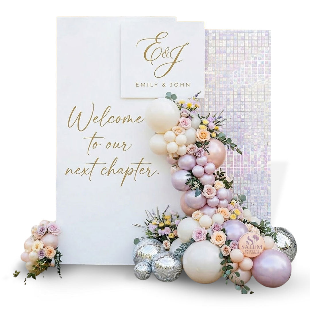 A cascading balloon and floral garland in pastel pink, peach, blush, and soft lavender flows down between the panel and a matching white iridescent shimmering sequin wall on a white background by Salem Balloons and Flowers.