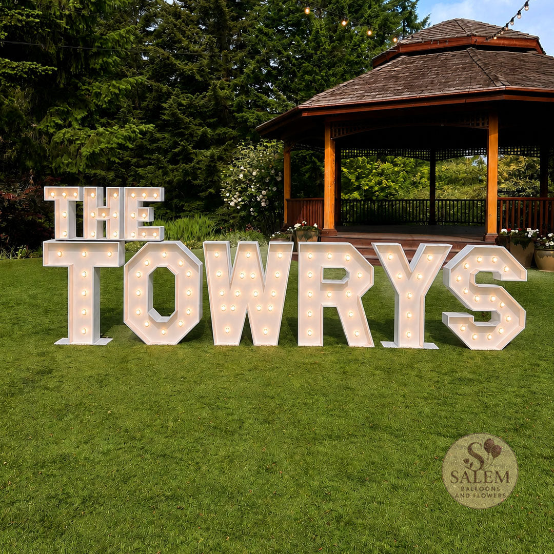 Decorative light-up letters spelling 'THE TOWRYS' in a garden setting with a gazebo. Wedding Marquee Letter Display. Event Decor Oregon.