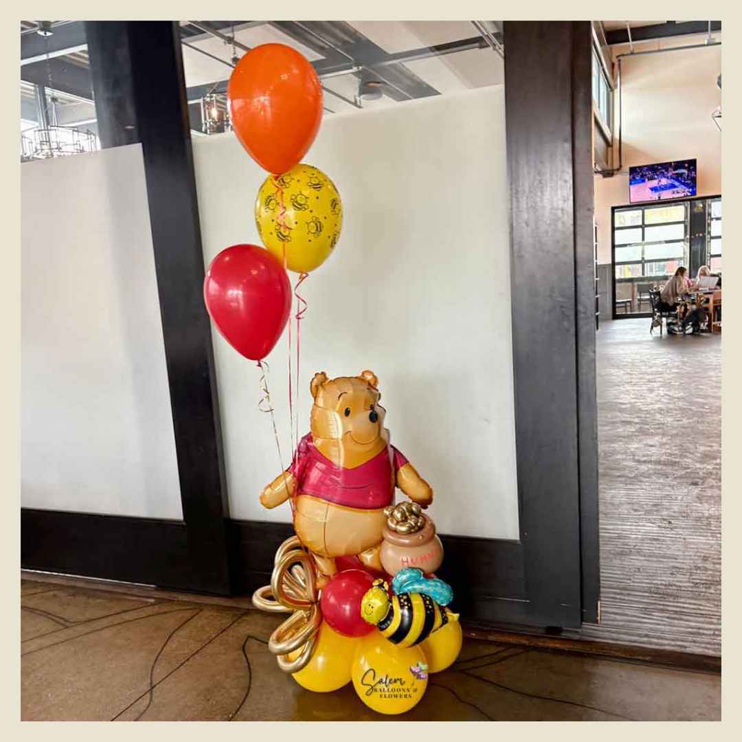 a Winnie the Pooh themed balloon bouquet with a large Winnie mylar balloon holding a honey pot filled with honey and bees. Oregon Balloon Delivery.