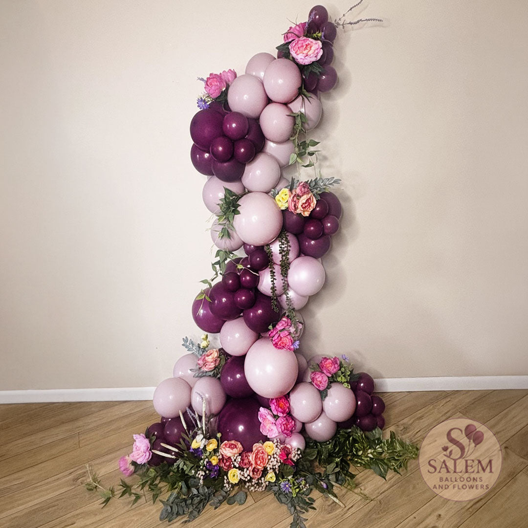 Organic balloon garland in a zig zag shape in dusk pink, grape purple and embellished with flowers and greenery ideal for bridal shower, baby shower, birthdays, by Salem Balloons and Flowers.